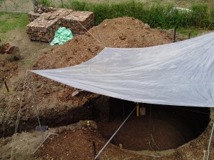 A tarp placed over the hole to keep out the rain. Bricks to be used for the walls in the background.